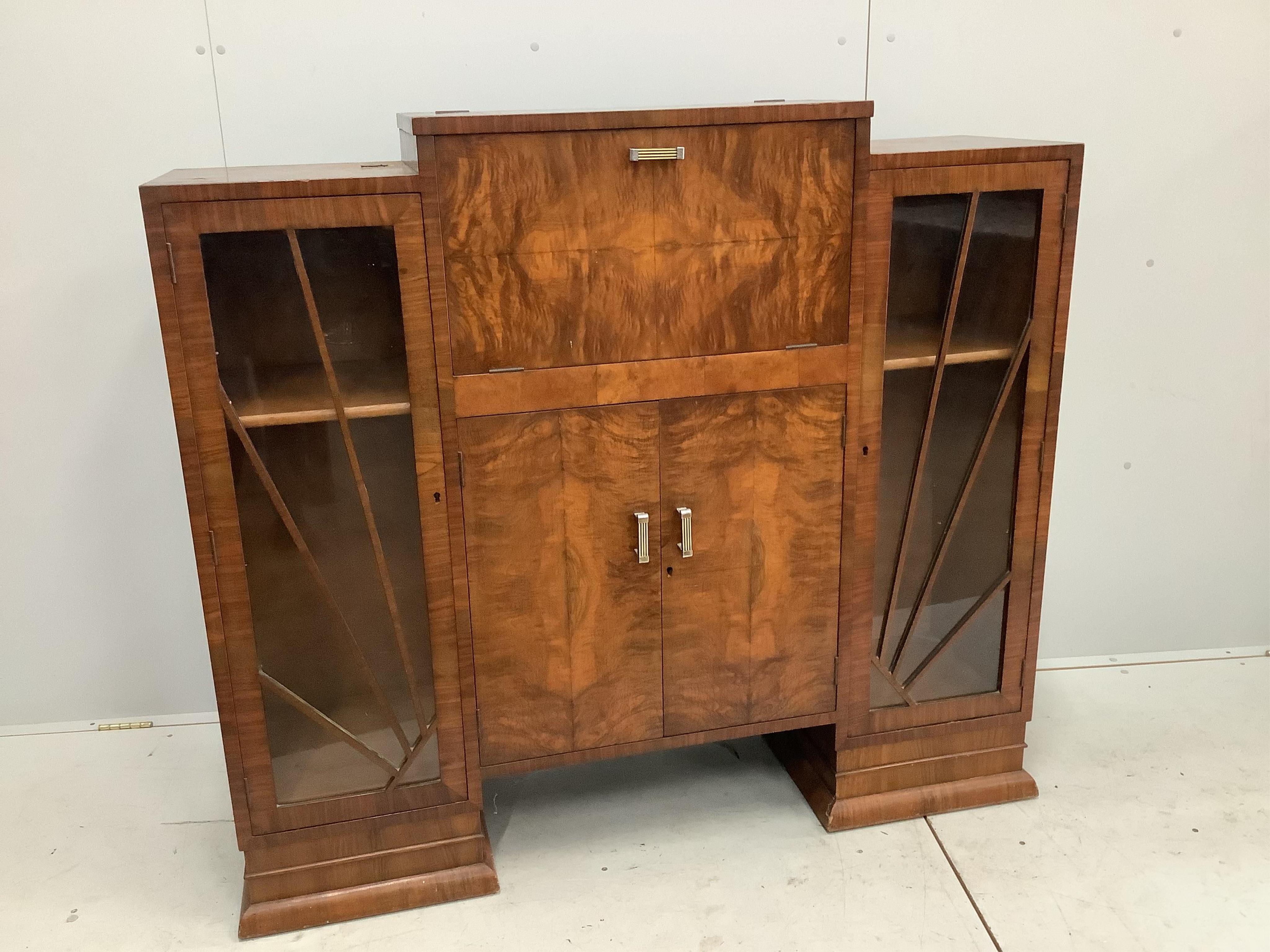 An Art Deco figured walnut cocktail cabinet, width 136cm, depth 39cm, height 123cm. Condition - one glass panel missing, otherwise fair